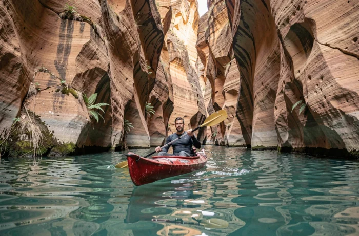 Homme en kayak rouge pagayant dans un canyon de grès lors d'une aventure en eaux vives